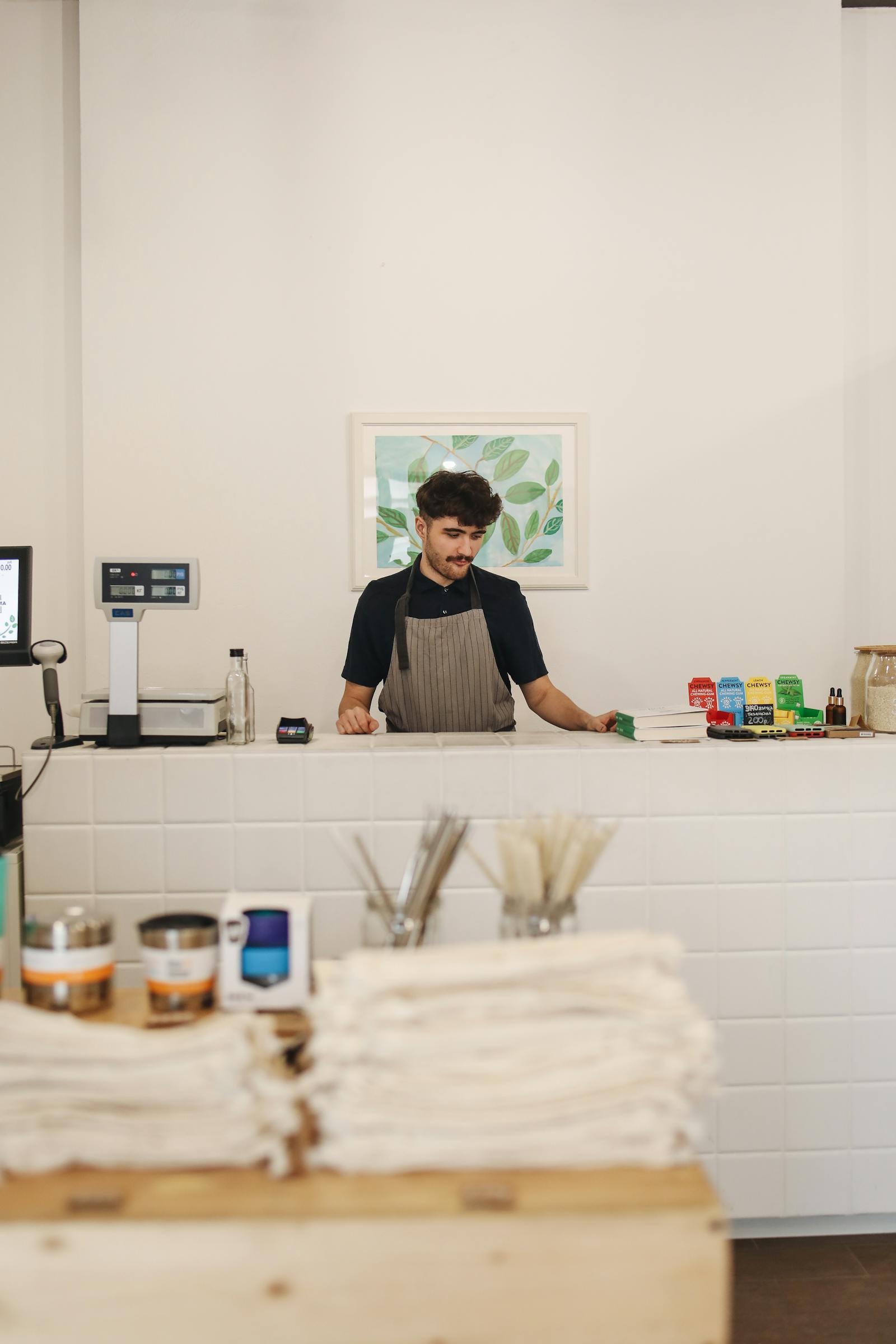 Shopkeeper working at a retail counter with a card reader and barcode scanner nearby.